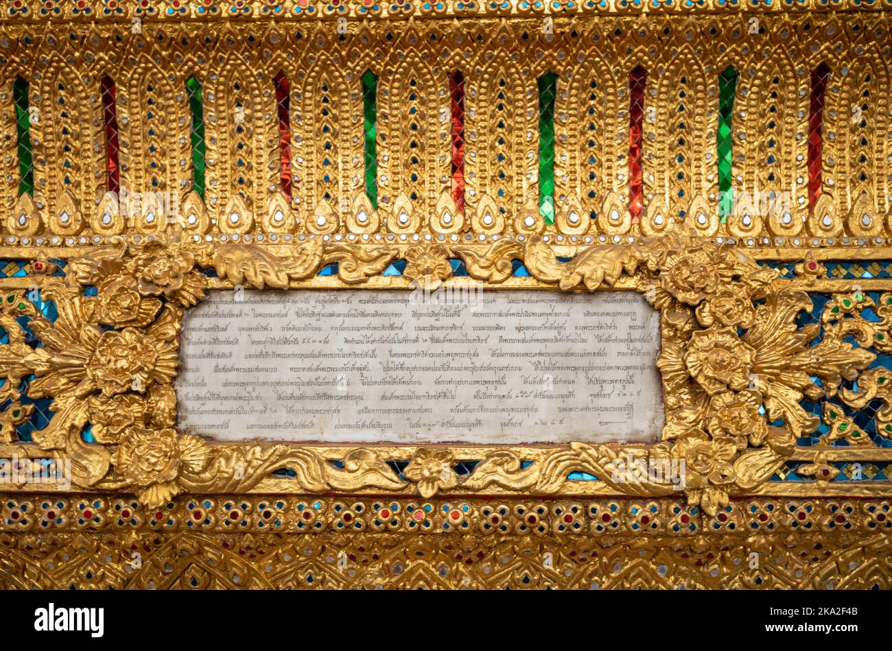 Una targa con scritta thailandese circondata da intricate decorazioni dorate e colorate all'esterno di un tempio a Wat Arun, o il Tempio dell'Alba, a Ban Foto Stock