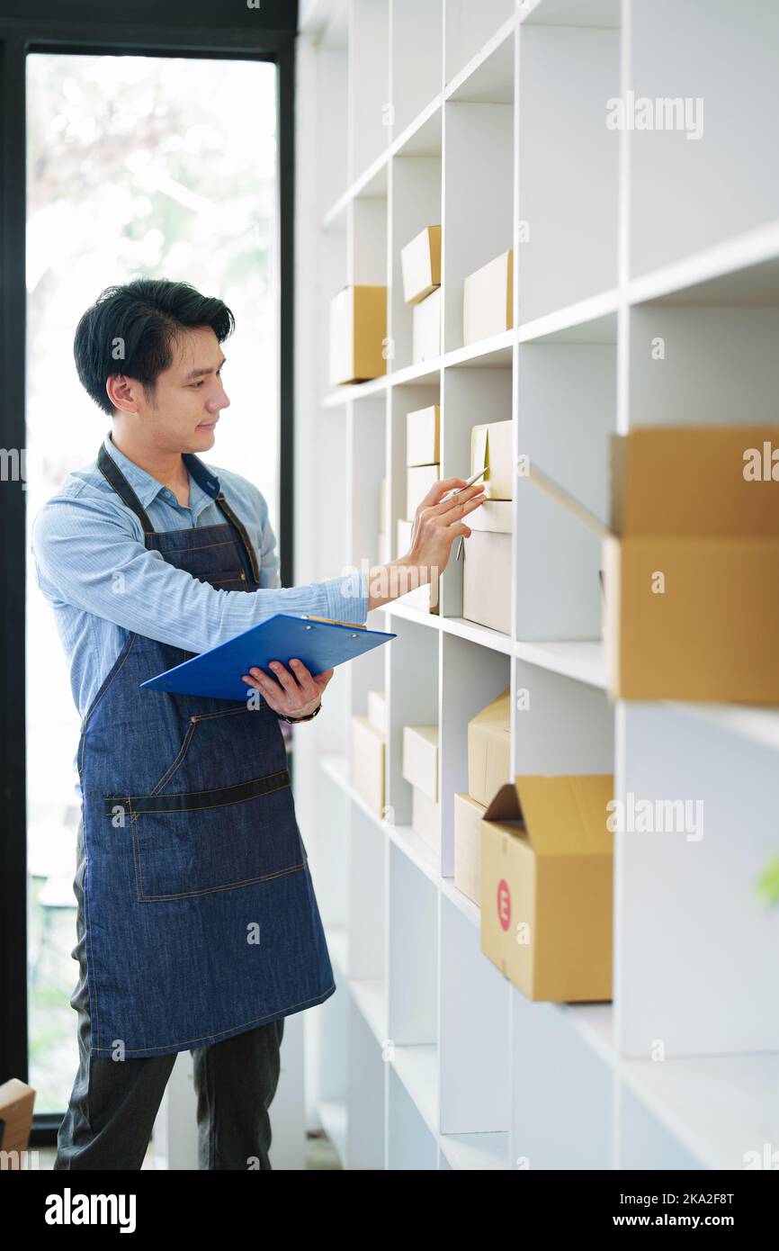Un ritratto di una piccola startup, un proprietario di PMI, un imprenditore asiatico maschio che controlla gli ordini per organizzare il prodotto prima di imballare i prodotti nel Foto Stock