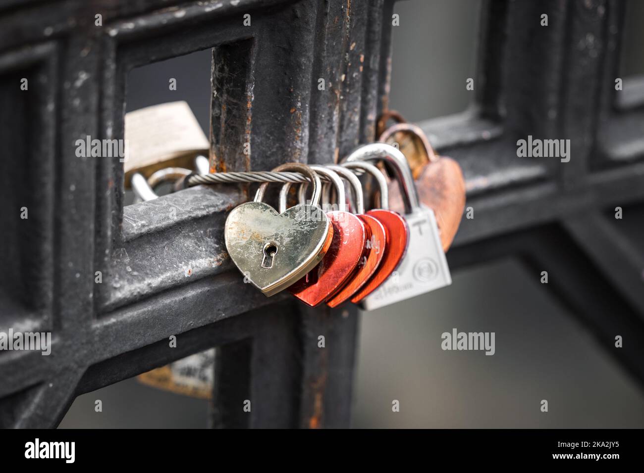 Serrature Love collegate al ponte. Lucchetto in ottone rosso con cuore d'amore fissato a barre di metallo su ponte. Foto Stock