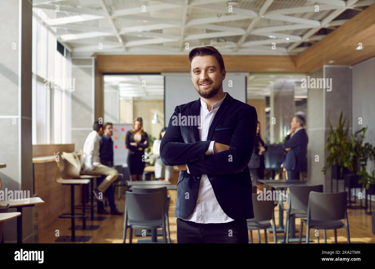 Ritratto di un uomo d'affari positivo millenario che si pone sullo sfondo di un ufficio moderno. Foto Stock