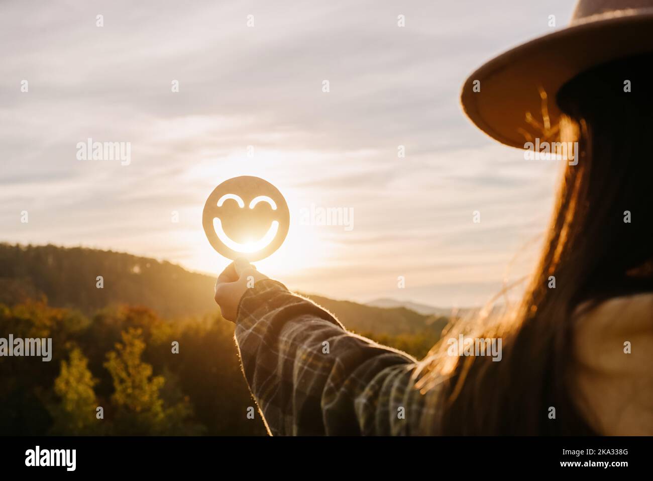 Primo piano di una giovane donna che tiene allegro sorriso emoticon sullo sfondo bellissimo tramonto in montagna il giorno d'autunno. Immagine positiva o vita felice, WO Foto Stock