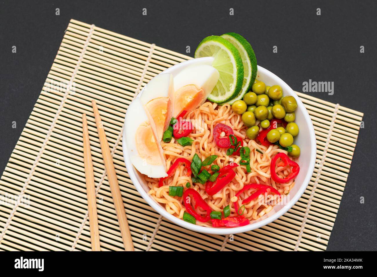 Bellissima pasta con piselli verdi, uova, peperoncino rosso, verdure e lime con chopsticks su un piatto di sushi. Tagliatelle istantanee Foto Stock
