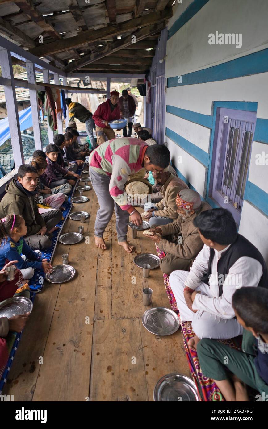 La gente che siede su una veranda di legno ed è servita il cibo in un villaggio himalayano nell'India del Nord. Foto Stock
