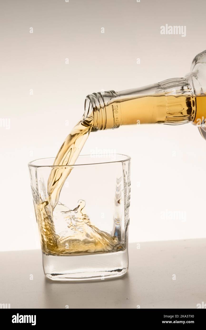 versare il whiskey o il bourbon in un bicchiere su uno sfondo bianco beige verticale. Foto Stock