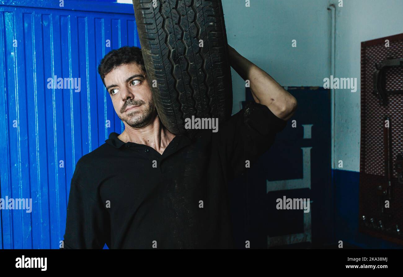 Meccanico con pneumatico auto in officina Foto Stock