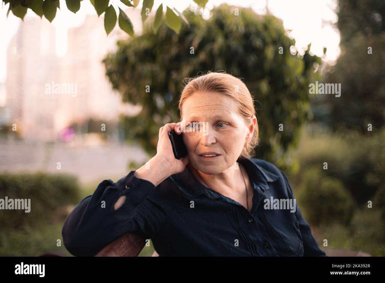Donna d'affari matura che parla sullo smartphone seduto sul panca in città Foto Stock