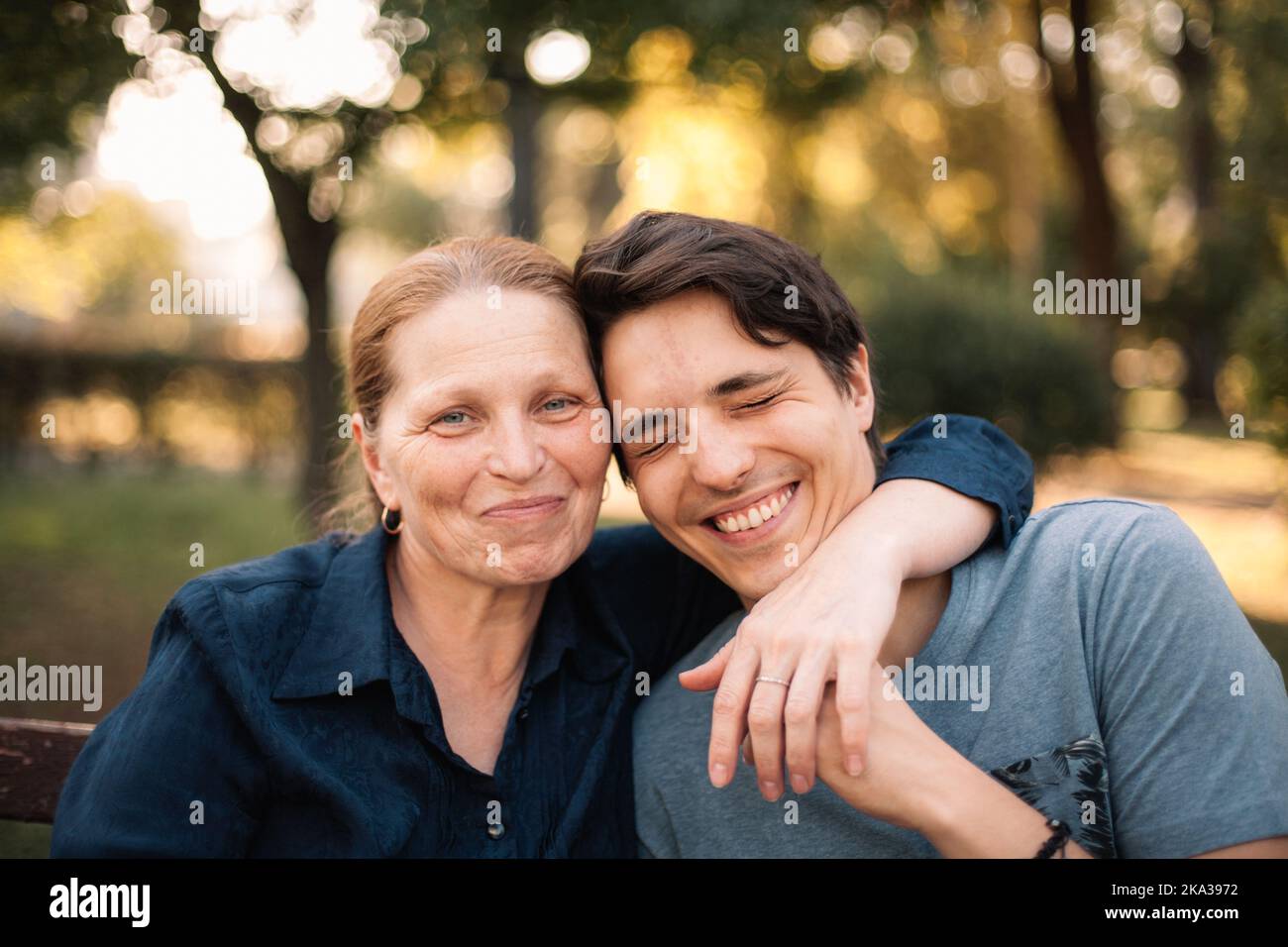 Felice madre matura che abbraccia sorridente figlio adulto nel parco in estate Foto Stock
