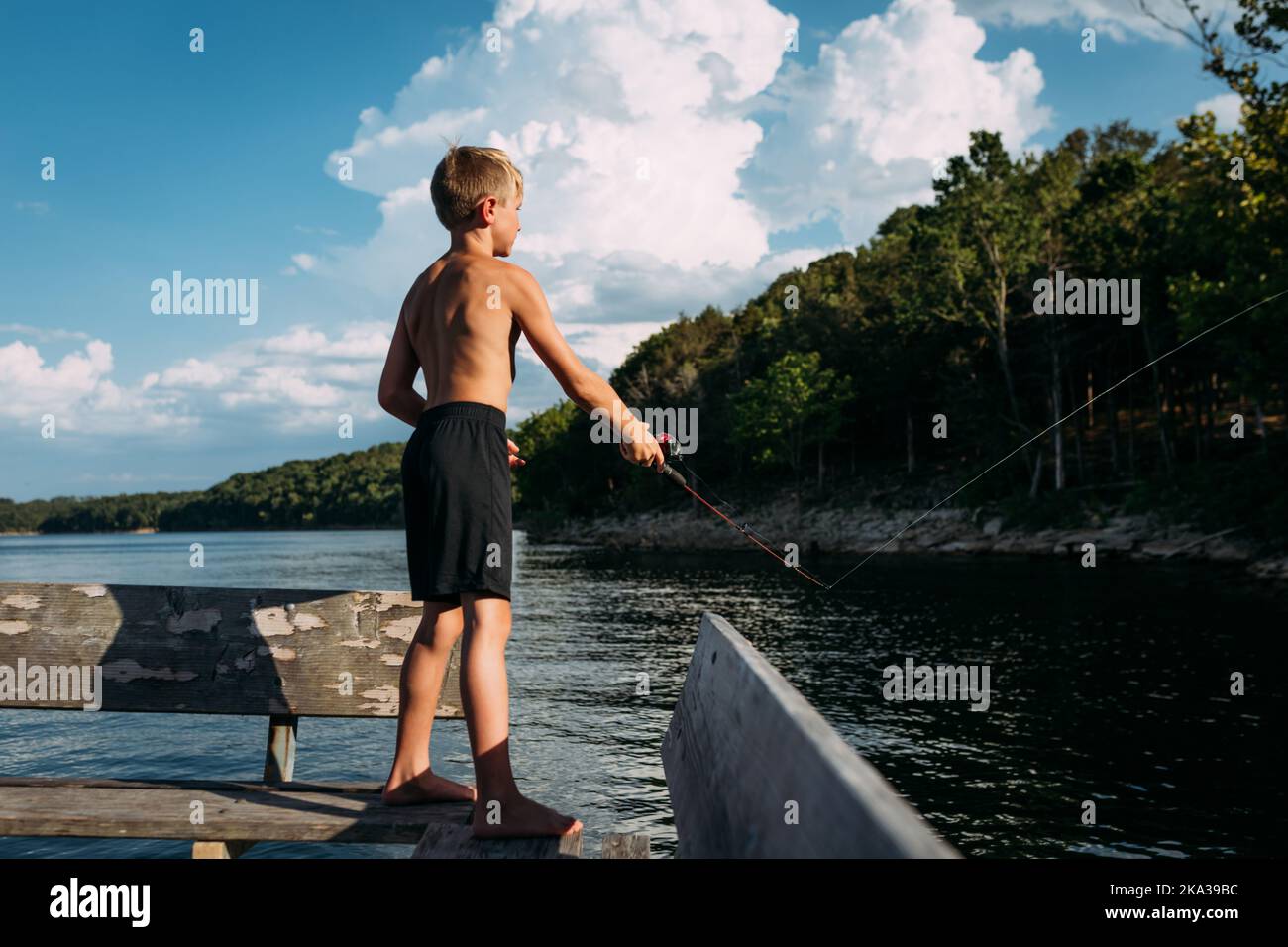 Giovane ragazzo che pesca al largo del molo nella soleggiata giornata estiva Foto Stock