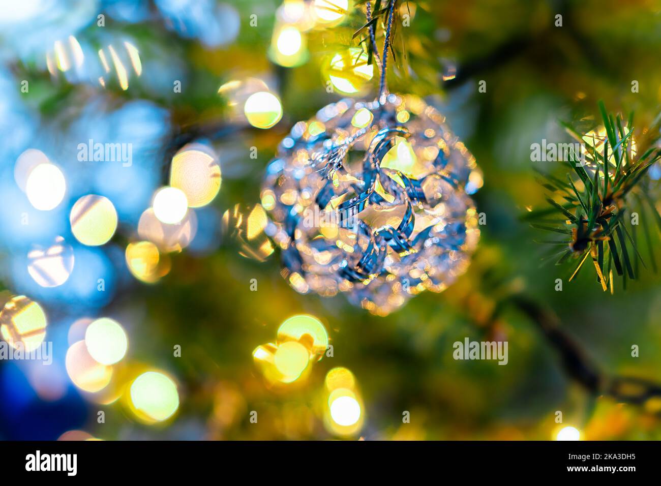 Macro primo piano di colorato ornamento decorativo giallo blu appeso all'albero di Natale di Capodanno con luci in inverno con cerchi bokeh dentro Foto Stock