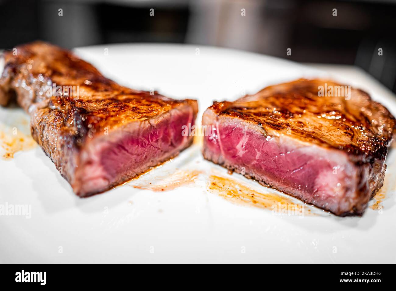 Macro primo piano di rara bistecca di manzo di carne alla griglia rossa cotta e alimentata con erba di New York tagliata in due metà con crudo all'interno su piatto bianco Foto Stock