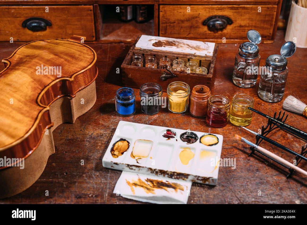 Dall'alto tavolo in legno con vernici e olio vicino al mix palette e violino in bottega di luziatore Foto Stock