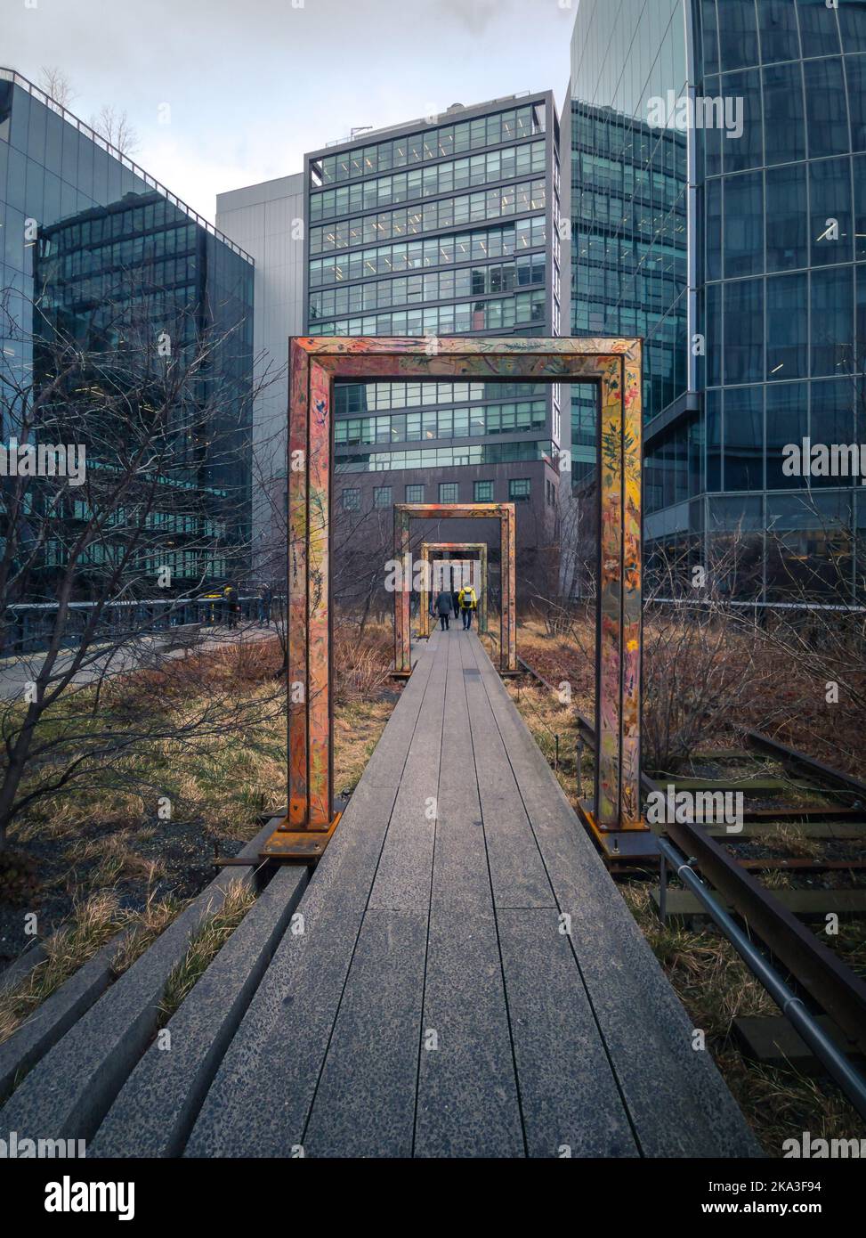 Percorso dritto con persone che vanno sotto archi rettangolari vicino a edifici moderni con pareti di vetro nel parco High Line a New York, USA Foto Stock