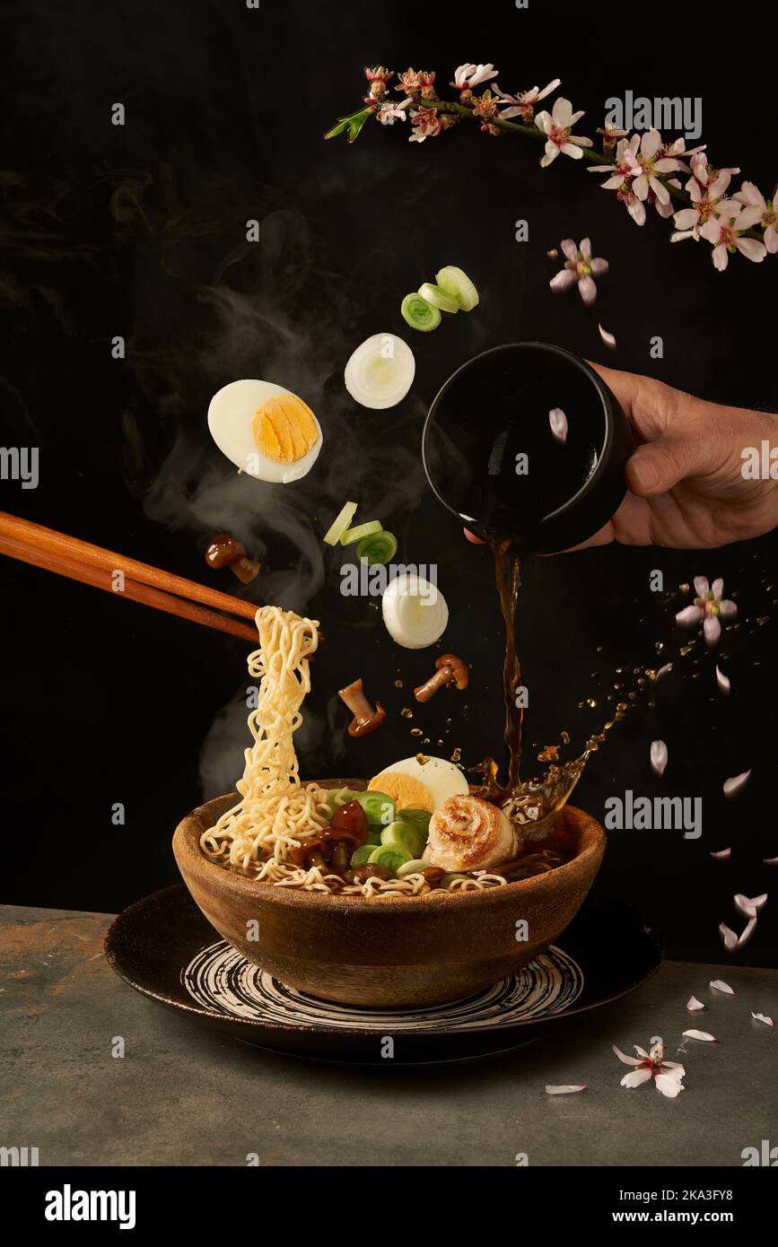 Cuocete le tagliatelle con i bastoncini e aggiungete il brodo miso al ramen, mentre le uova e la cipolla con i funghi cadono in una ciotola Foto Stock