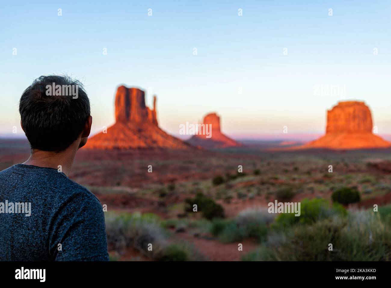 Un uomo indietro in piedi pov guardando la vista delle famose buttes nella Monument Valley al tramonto luce colorata in Arizona con rocce e piante di colore rosso arancio Foto Stock