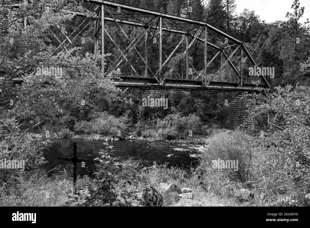 Un colpo in scala di grigi di un ponte sul fiume freddo circondato da alberi Foto Stock
