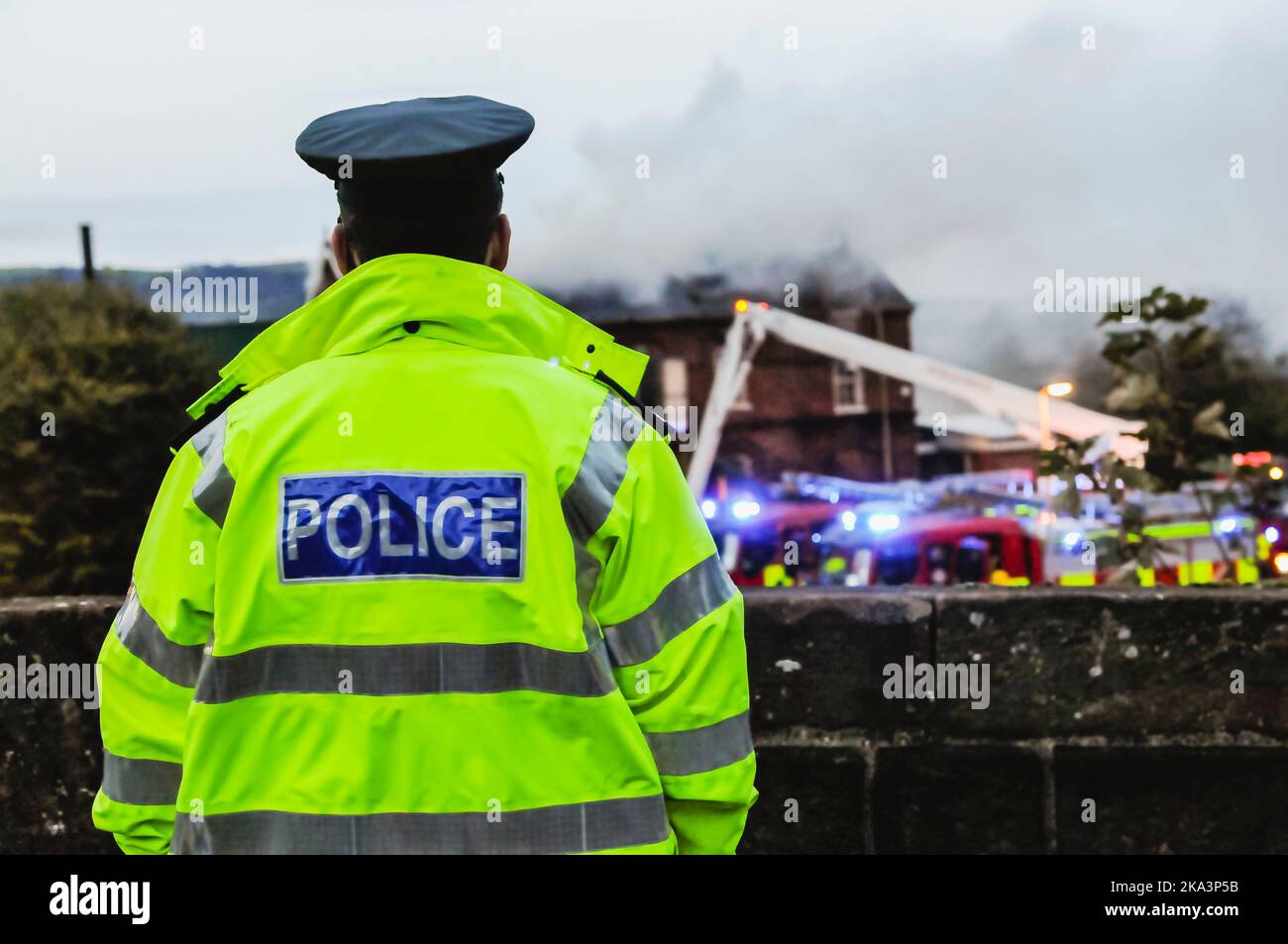 Un poliziotto che indossa una giacca ad alta visibilità guarda un vigile del fuoco che si trova in un vecchio edificio scolastico Foto Stock