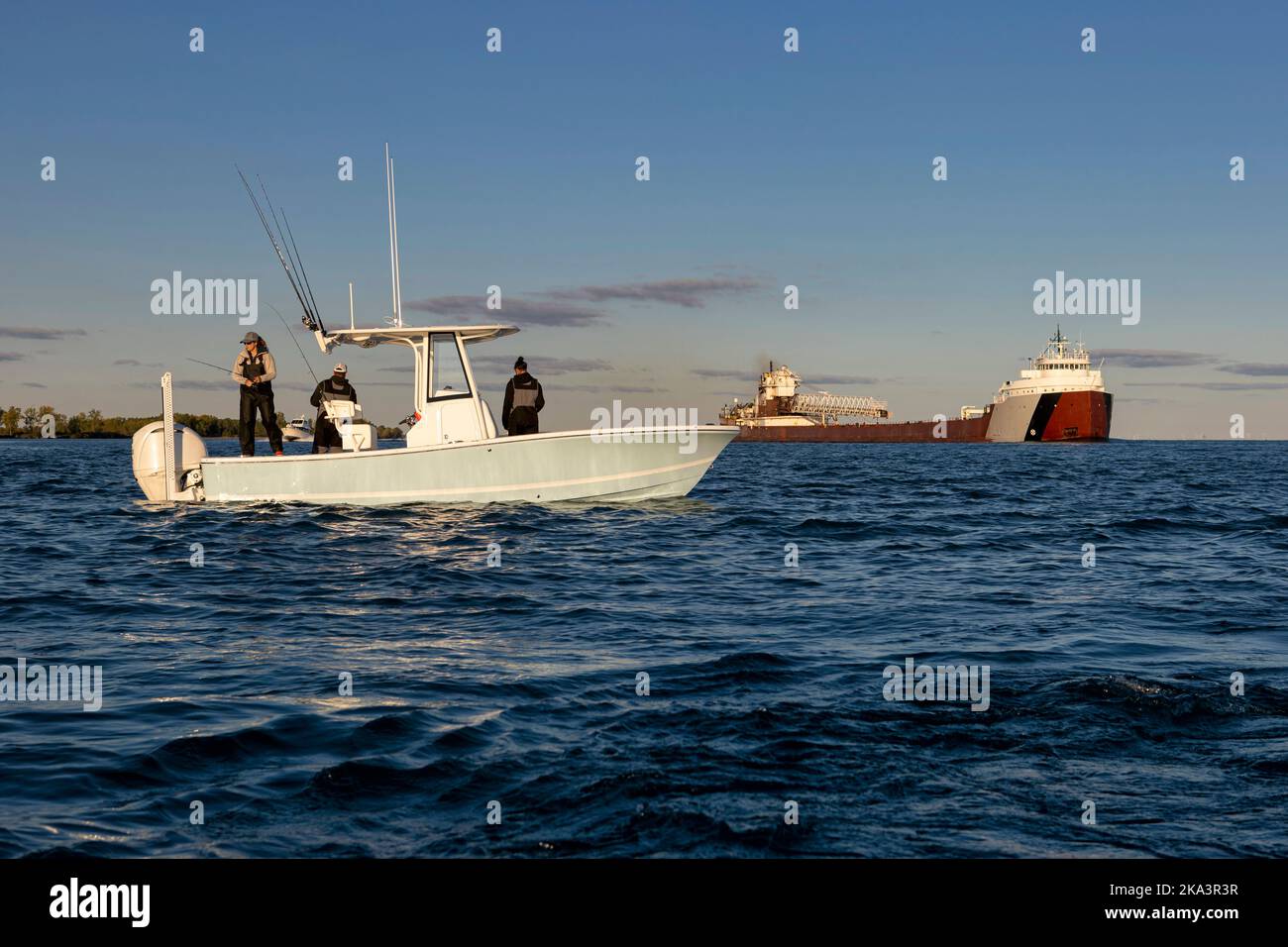 Persone che pescano su una barca con una grande nave sullo sfondo. Foto Stock