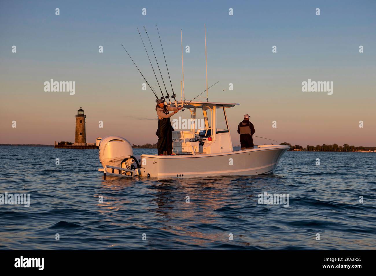 Persone che pescano su una barca con un faro sullo sfondo. Foto Stock