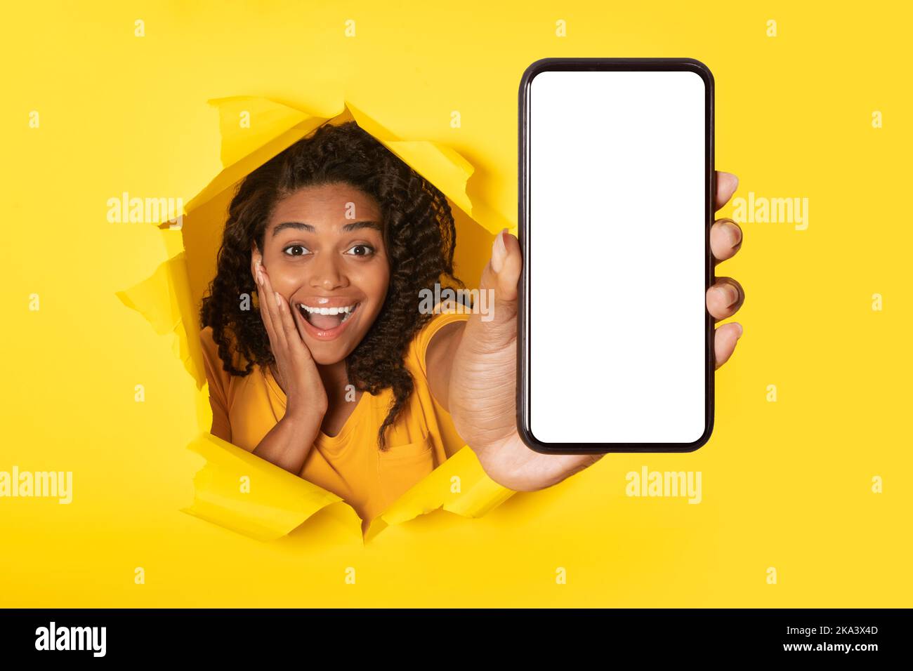 Donna nera allegra che mostra lo schermo del telefono attraverso la carta gialla strappata Foto Stock