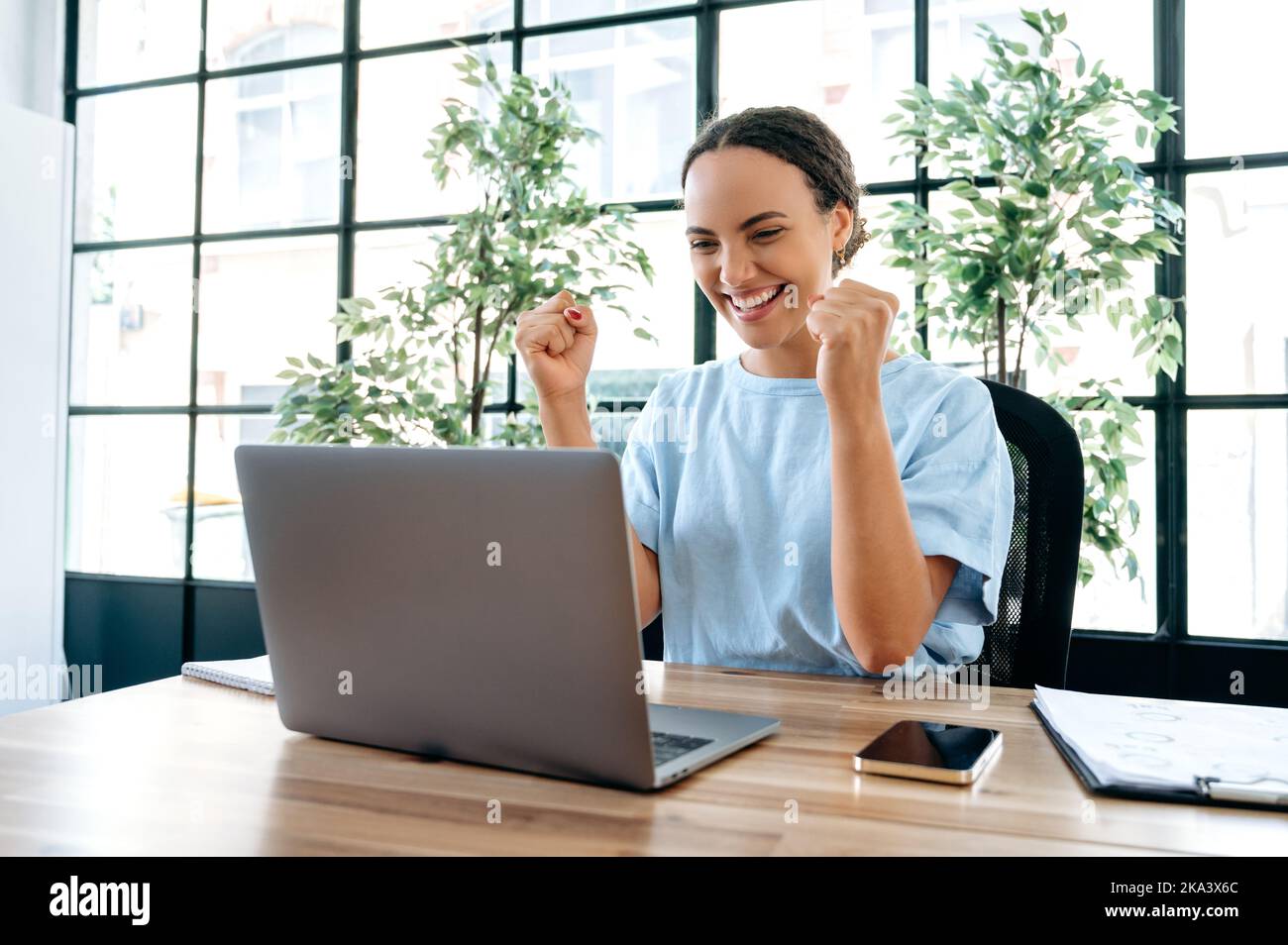 Stupito felice brasiliano o donna ispanica business, sedersi a una scrivania con notebook in ufficio moderno, gioire nel successo, grande profitto, celebrare l'affare, promozione di lavoro, pugni gestanti, guarda la fotocamera, sorride Foto Stock