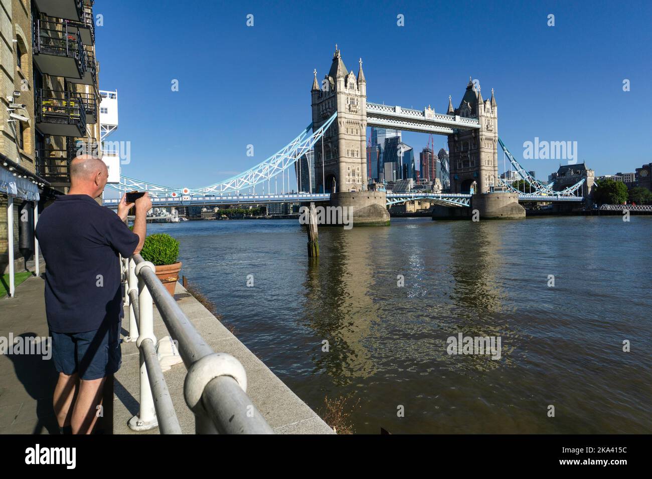 Vista posteriore di un uomo che fotografa il Tower Bridge da Butler's Wharf, Londra, Inghilterra, Regno Unito Foto Stock
