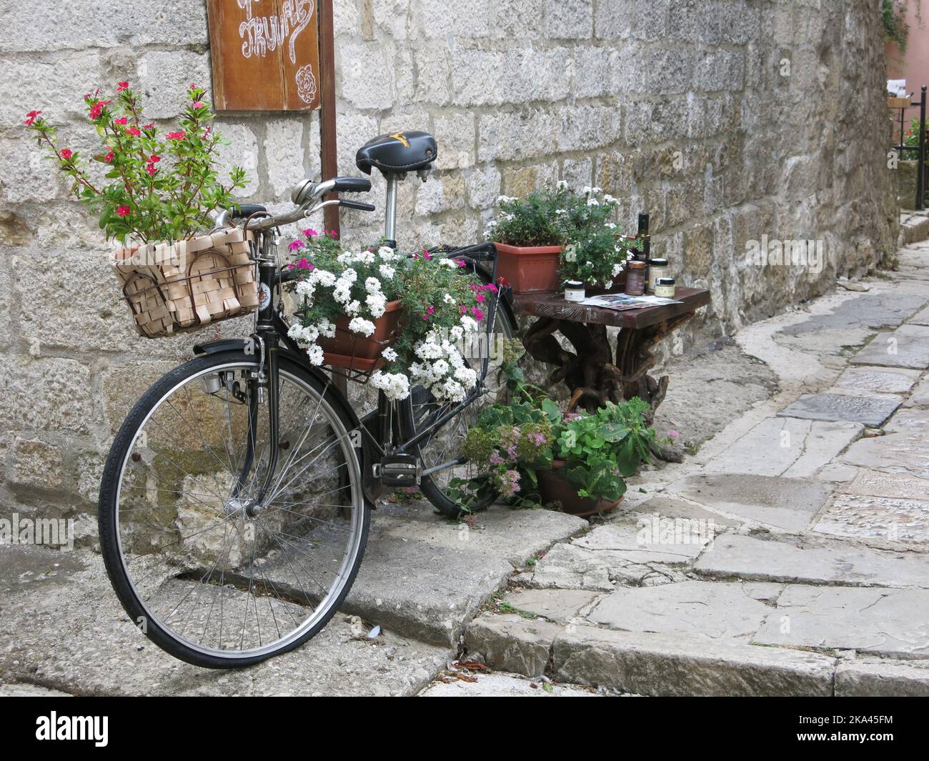Visita la Croazia: Un grazioso angolo di strada mentre cammini intorno alla città collinare di Motovun con una bicicletta abbarbicato in vasi di piante fiorite estive Foto Stock
