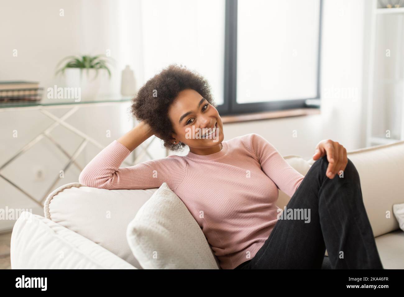 Allegro rilassato giovane afroamericana con capelli ricci sogno, si siede sul divano gode silenzio Foto Stock