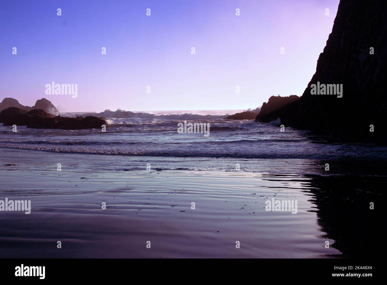 All'alba o al tramonto sulla costa dell'Oregon, con onde che si lavano su rocciatori ruvidi per raggiungere la spiaggia sabbiosa. Foto Stock