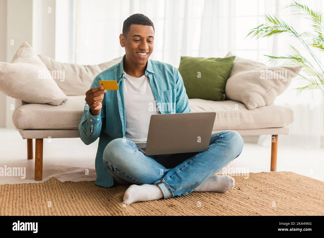 Nuovo ordine e online banking. Allegro giovane afro americano maschio con carta di credito e computer Foto Stock