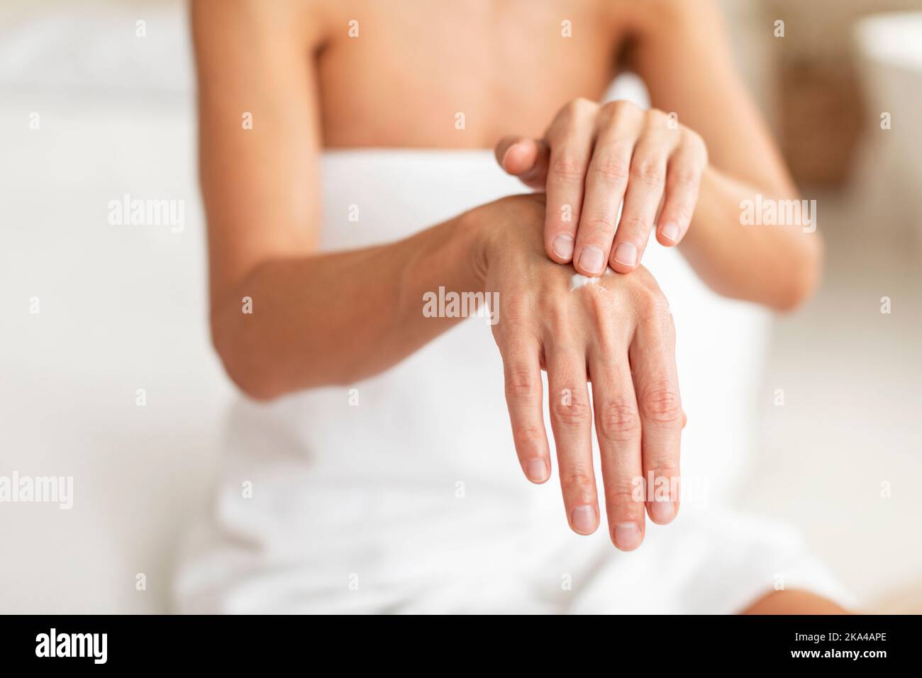 Colpo di primo piano di donna di mezza età applicando goccia di crema idratante sulle mani, utilizzando lozione nutriente per la pelle secca Foto Stock
