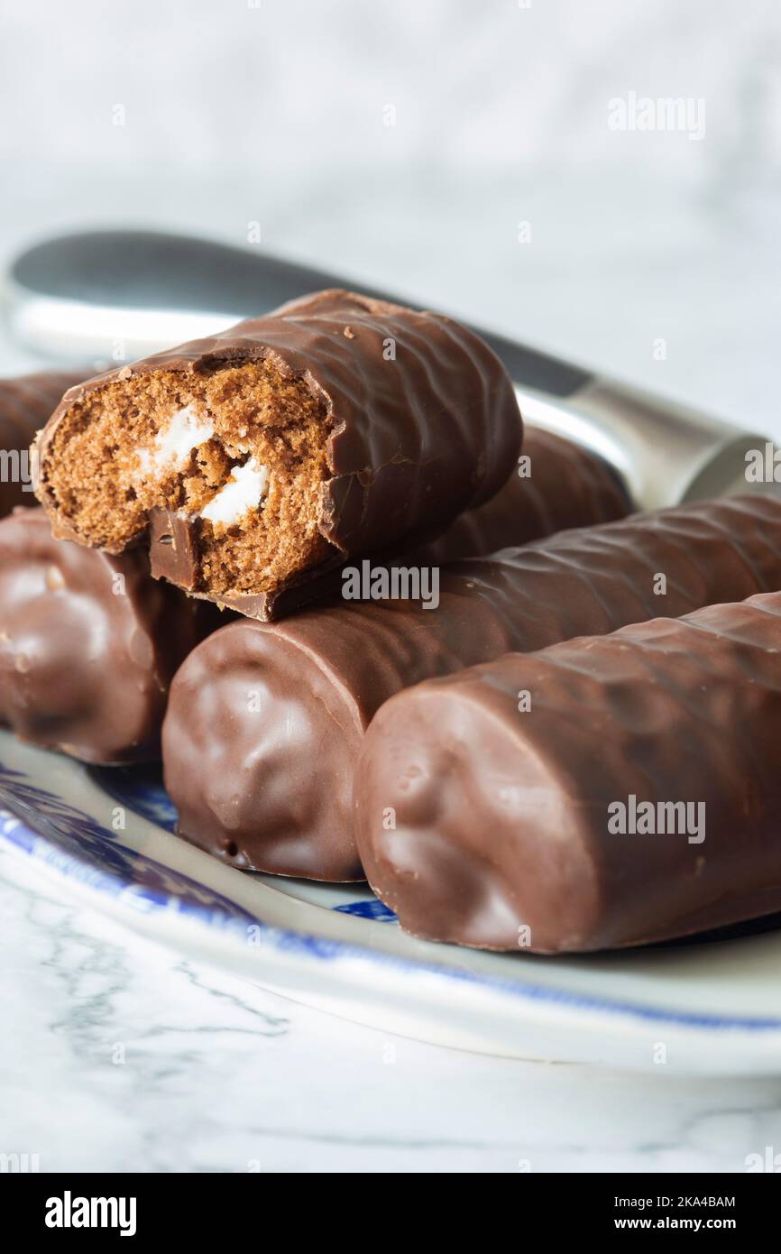 Rotoli di spugna al cioccolato individuali su un piatto blu e bianco a motivi geometrici con un coltello da portata. Su uno sfondo di marmo bianco Foto Stock