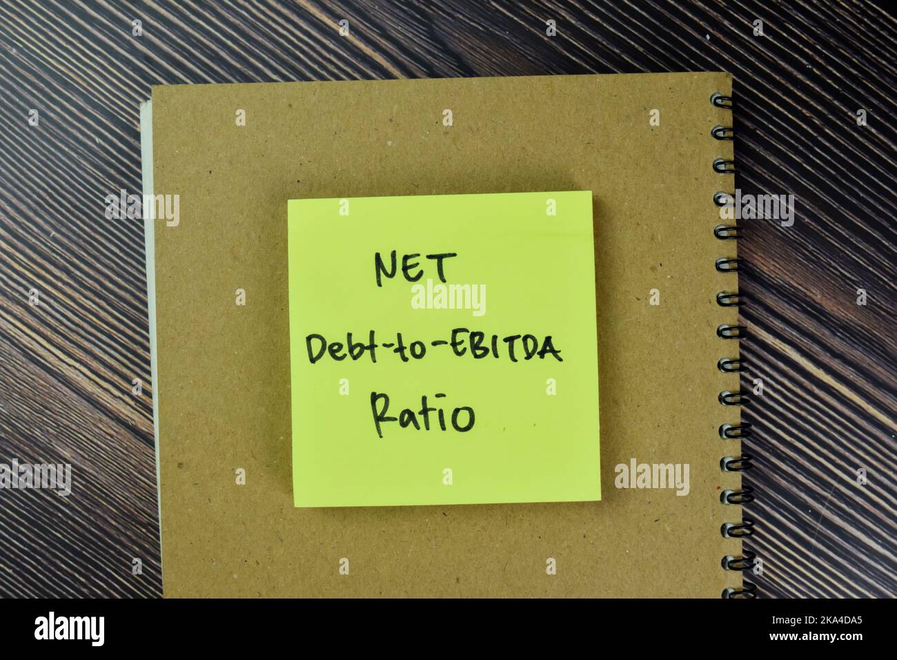 Concetto di rapporto debito-EBITDA netto scrivere su note appiccicose isolate su tavola di legno. Foto Stock