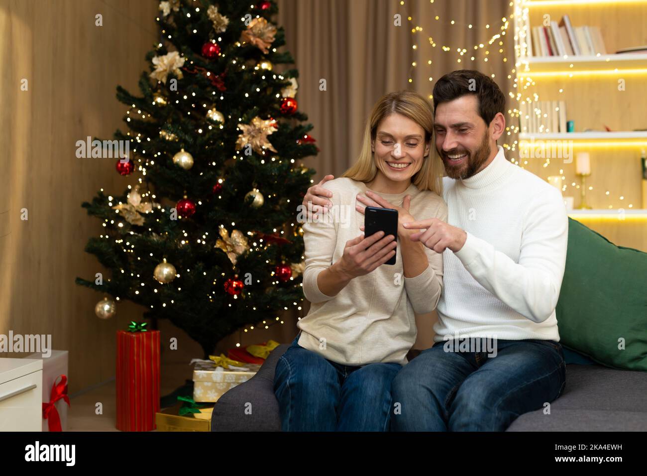 Coppia sposata scegliere regali di Natale in vacanza offerte online. Sposi amorevoli felici si siedono dall'albero luminoso di Capodanno. Foto Stock