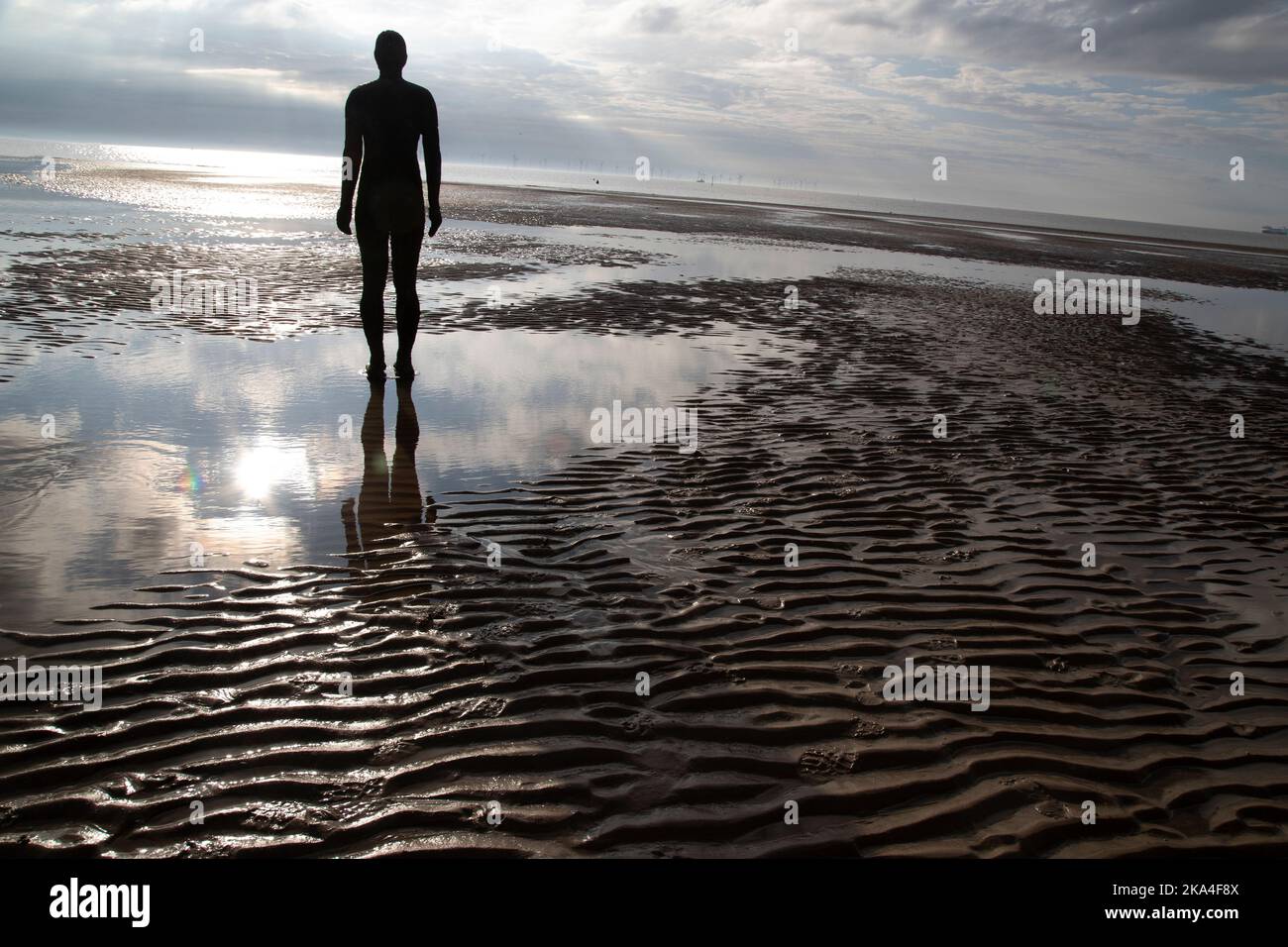 Una delle figure della scultura in ghisa di Antony Gormley di un uomo che guarda fuori al mare 'un altro posto' alla bassa marea a Crosby Beach, Merseyside, Regno Unito Foto Stock