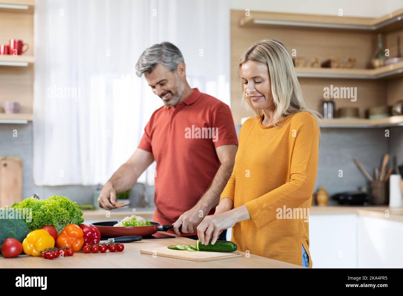 Sposi felici di mezza età che cucinano e che hanno conversazione Foto Stock