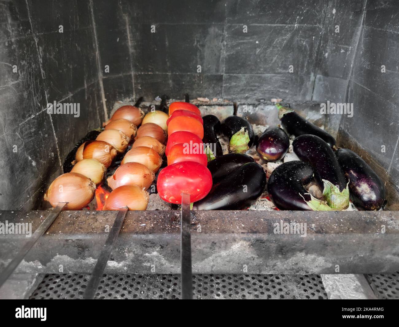 Le verdure crude sugli spiedini sono fritte sulle carboni. Cipolle, pomodori, melanzane alla griglia. Picnic Foto Stock