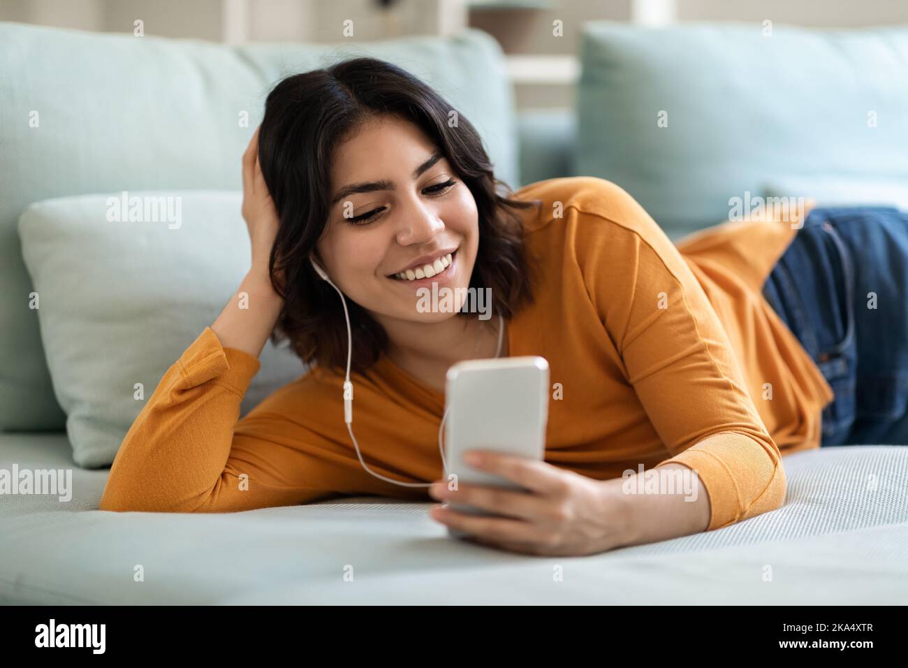 Ritratto di donna araba sorridente indossando auricolari rilassanti con smartphone a casa Foto Stock