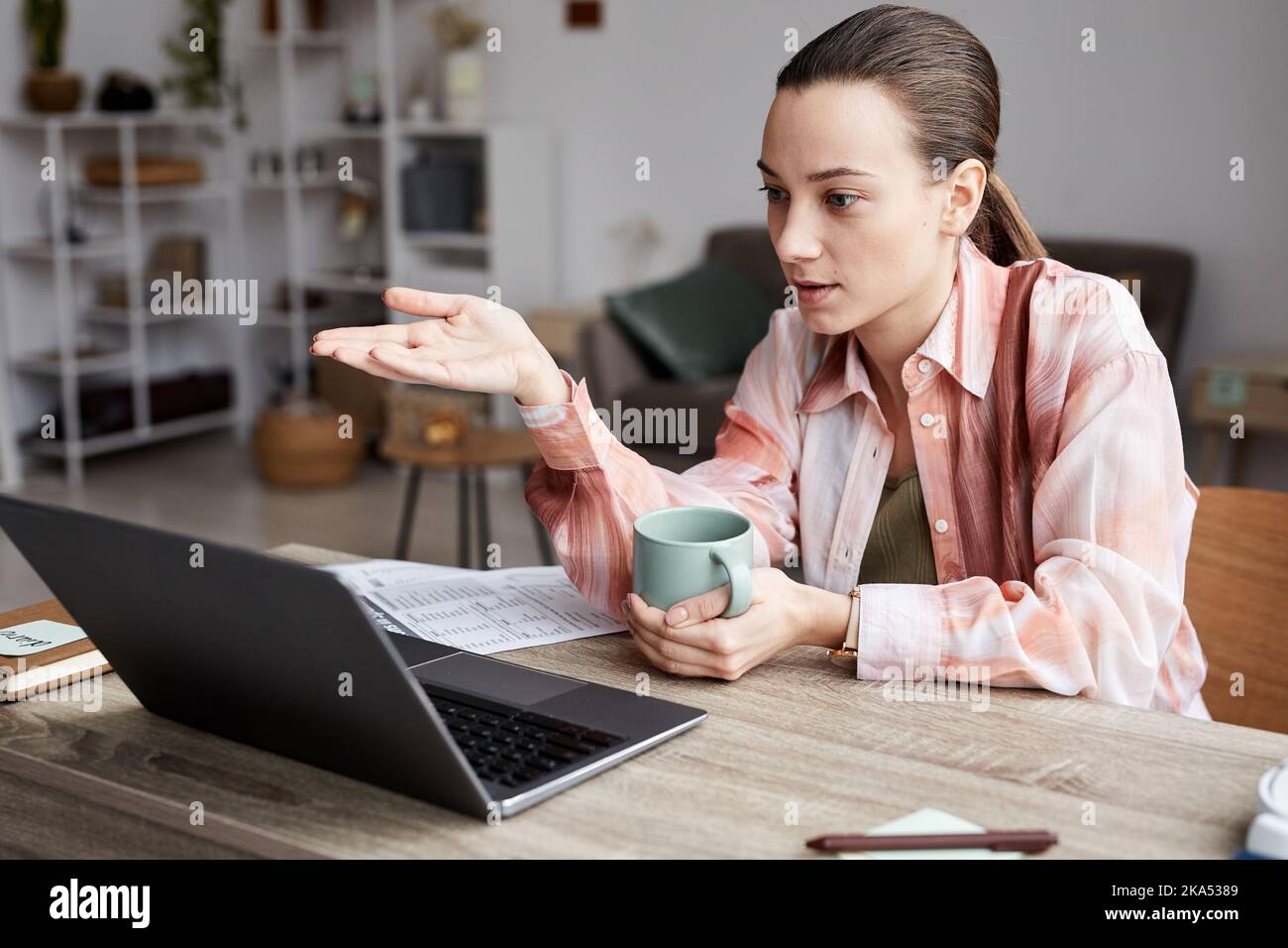 Un giovane tutor sicuro che spiega agli studenti online un nuovo argomento durante la lezione mentre si siedono alla scrivania di fronte al computer portatile a casa Foto Stock