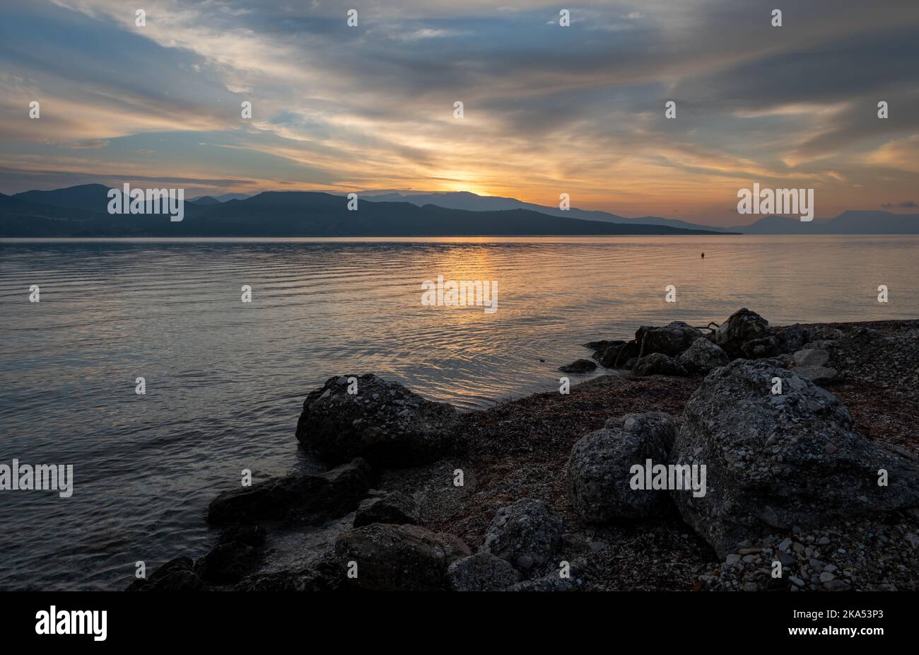 Il sole che sorge sopra la collina che proietta riflessi di luce dorata sul mare calmo. Foto Stock