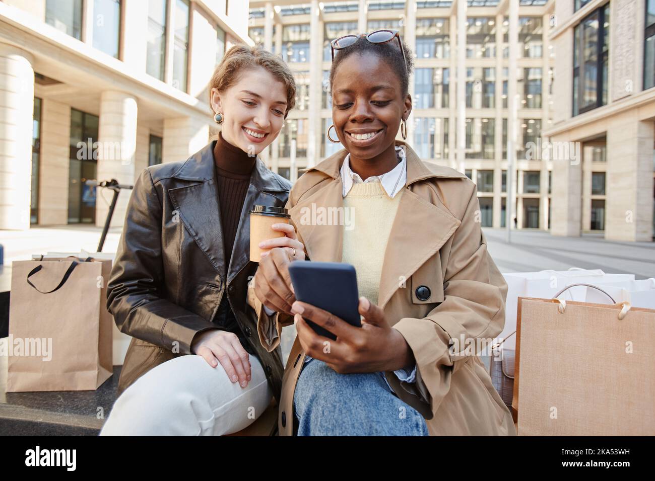 Ritratto di due giovani donne che usano lo smartphone dopo una giornata di shopping e sorridenti Foto Stock