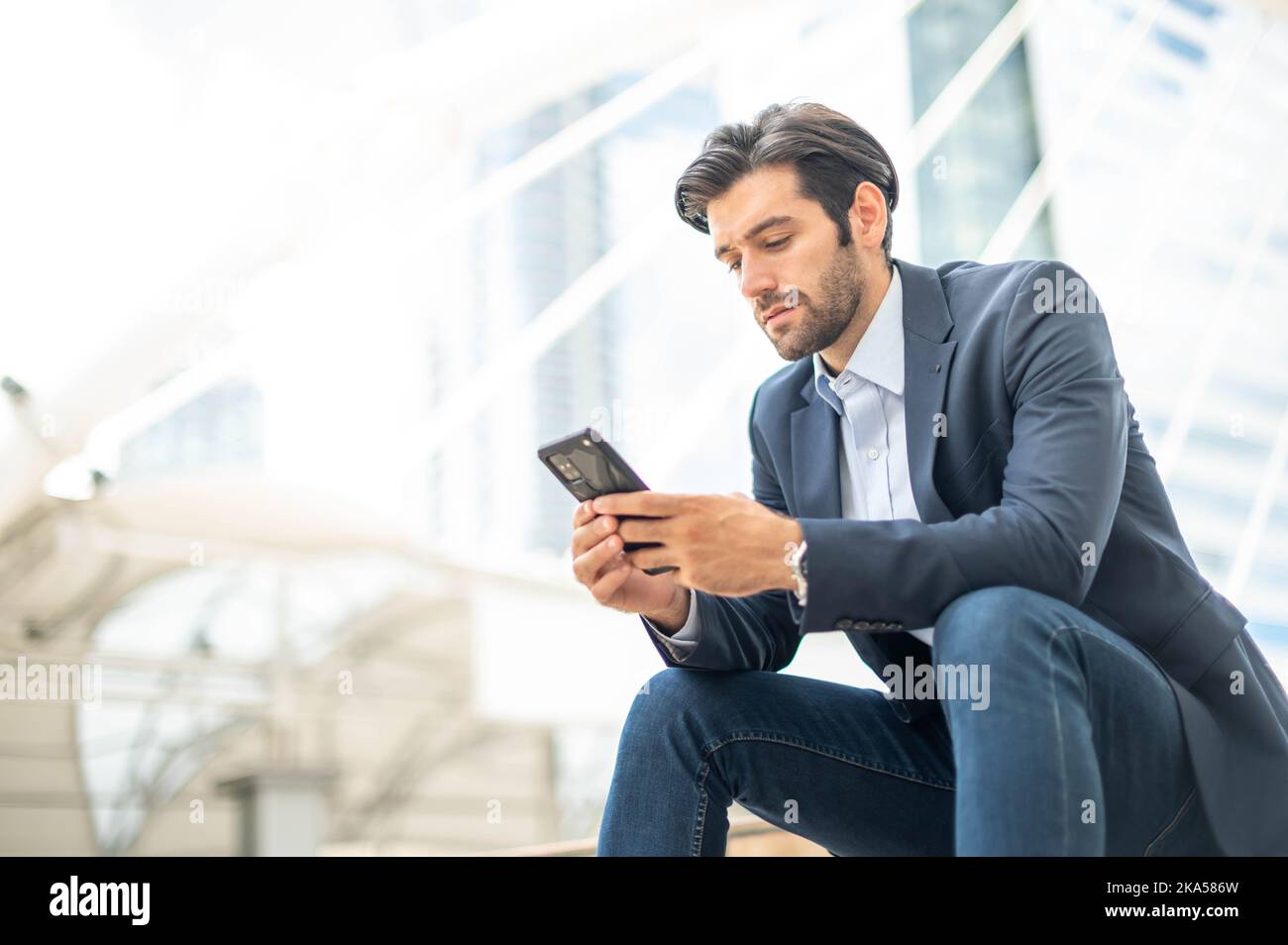 Primo piano di un giovane uomo serio caucasico che utilizza un moderno dispositivo smartphone mentre si siede in un'area pubblica. Foto Stock