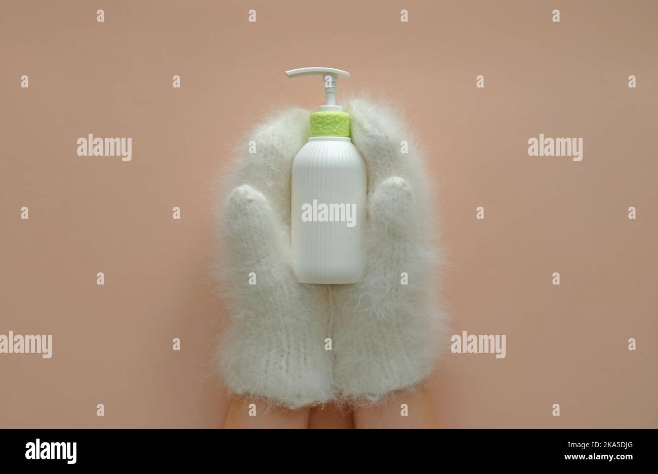 La bottiglia cosmetica della lozione idratante tiene le mani nei mitens. Foto Stock