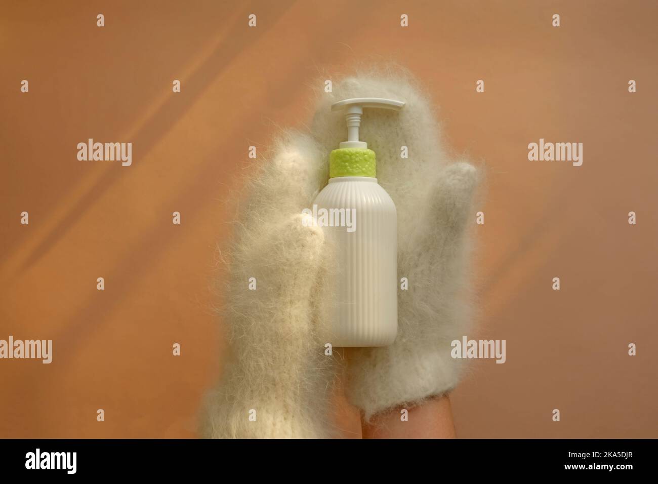 La bottiglia cosmetica della lozione idratante tiene le mani nei mitens. Foto Stock
