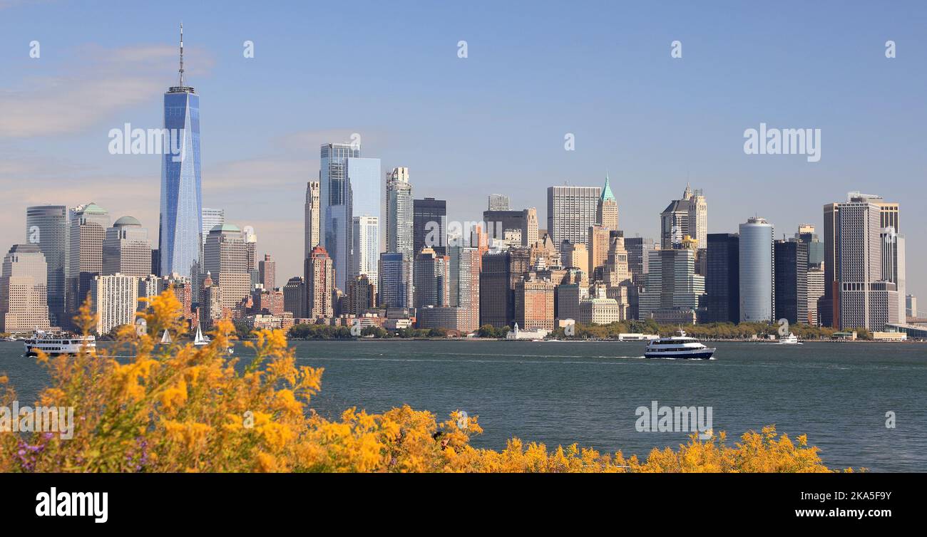 I grattacieli di New York City (Lower Manhattan) si ammirano dall'acqua, tra cui una barca e gli alberi gialli autunnali in primo piano, USA Foto Stock