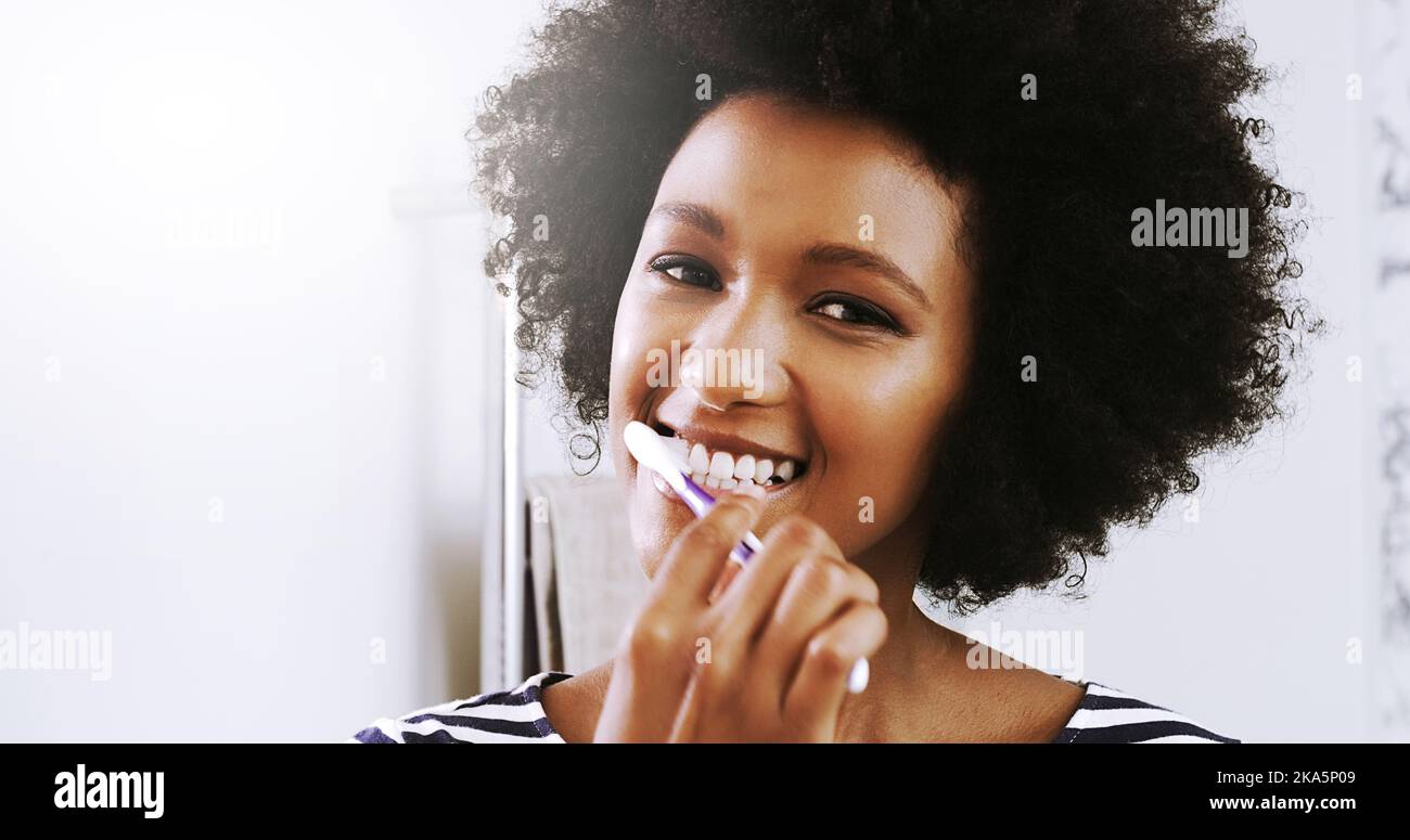 Routine mattutine. Ritratto di una giovane donna allegra che si strofinava i denti mentre guardava il suo riflesso nello specchio del bagno di casa. Foto Stock