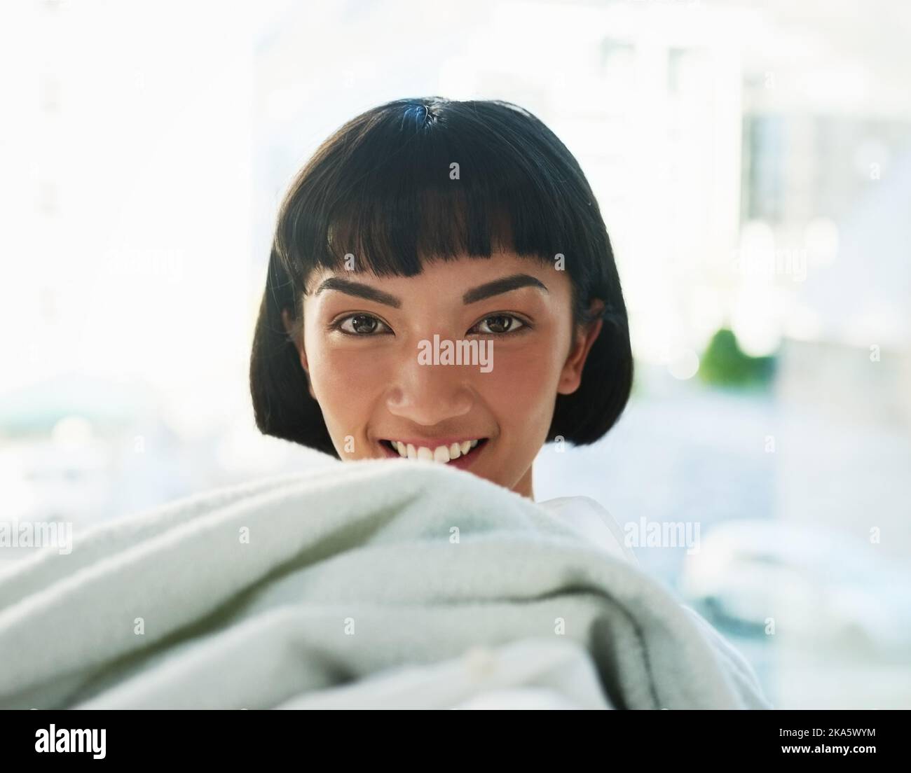Un carico fatto. Una giovane donna che trasporta un mucchio di asciugamani il giorno della lavanderia a casa. Foto Stock