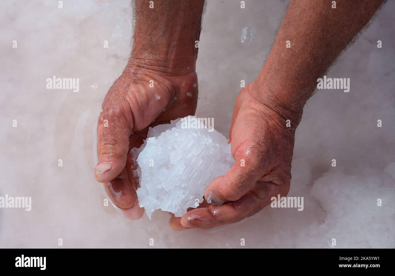 Mani di un lavoratore che raccoglie il sale in una padella di sale siciliana. Italia. Foto Stock