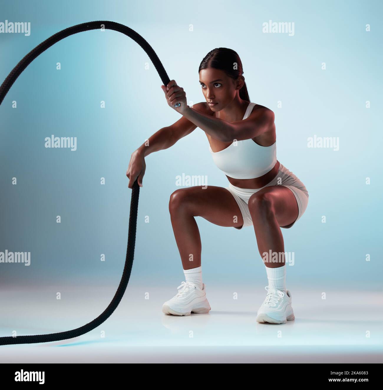 Donna, corda da battaglia e esercizio su sfondo blu in studio di resistenza allenamento, sport energetici o cardio allenamento. Personal trainer, modello di fitness o. Foto Stock