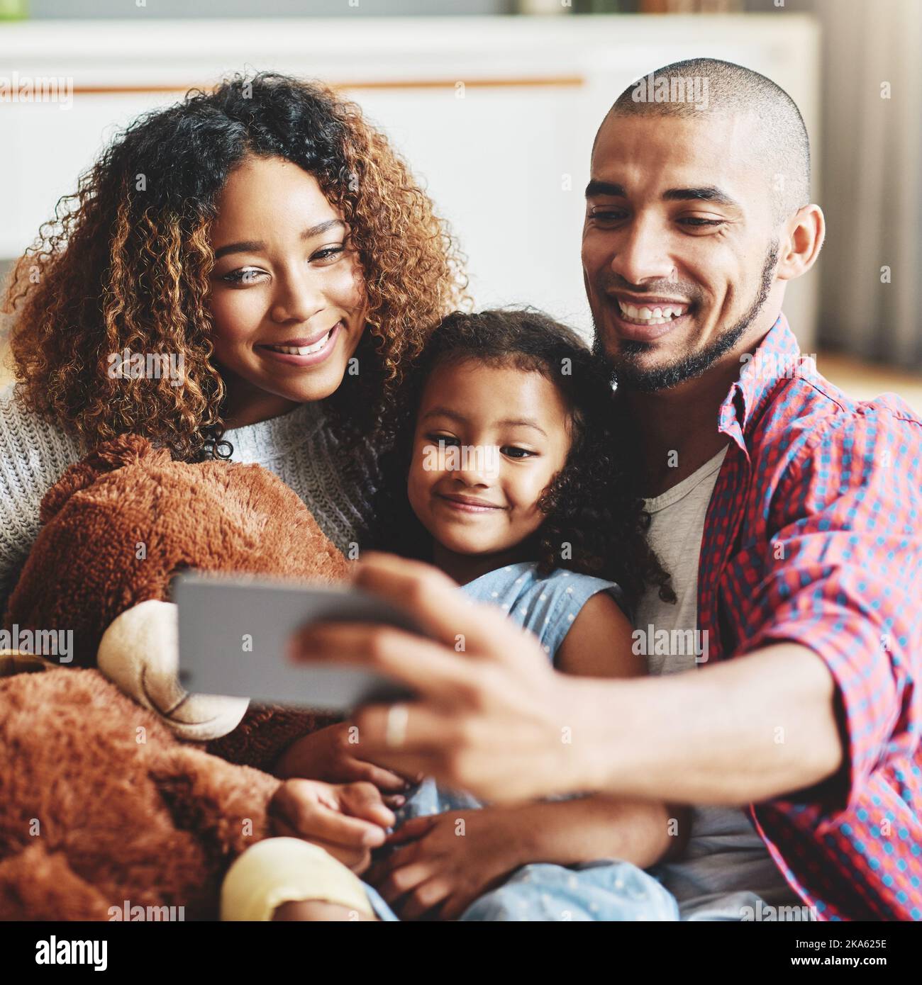 Sono semplicemente perfetti. Una famiglia giovane e felice di tre persone che prende selfie insieme nel proprio salotto di casa. Foto Stock