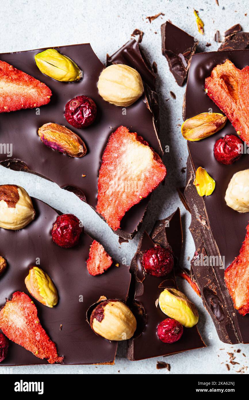 Cioccolato fondente vegano fatto in casa con frutti di bosco e noci su carta bianca, vista dall'alto. Foto Stock